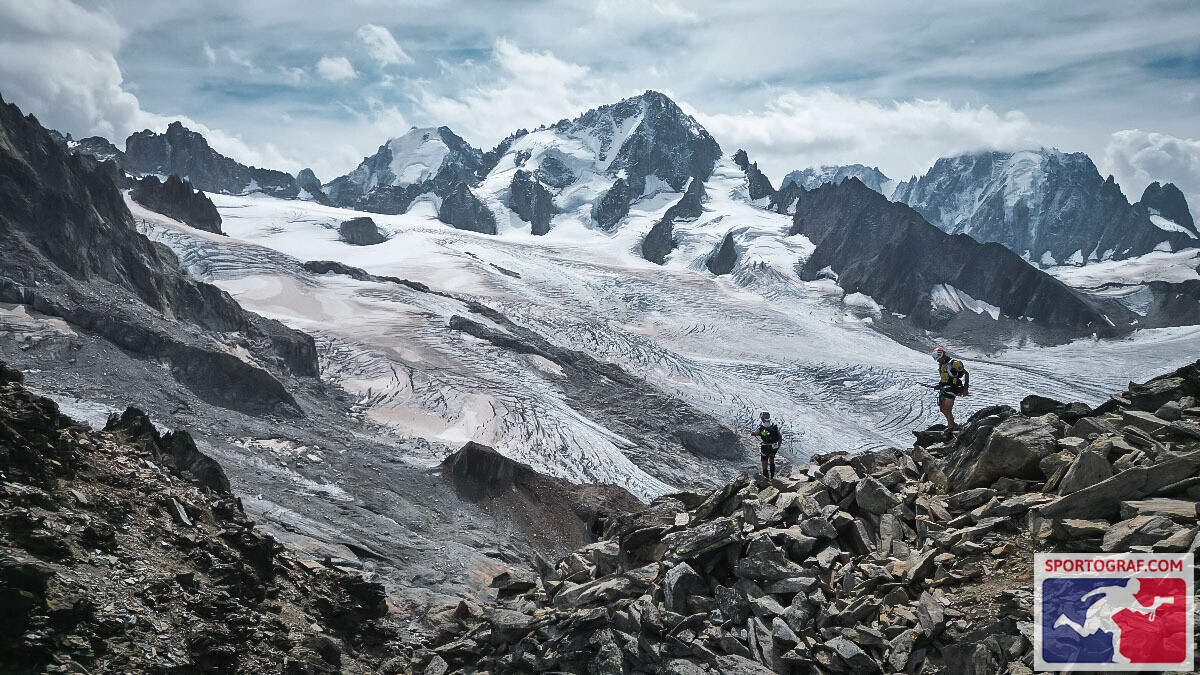 Trail runners crossing a rocky ridge above a glacier